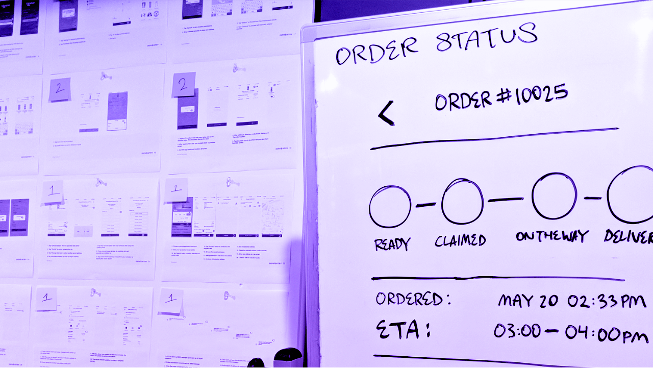 Dry erase board in the foreground displays sketched interface components while pinned sheets are labeled with numbered sticky notes on foamcore in the background.